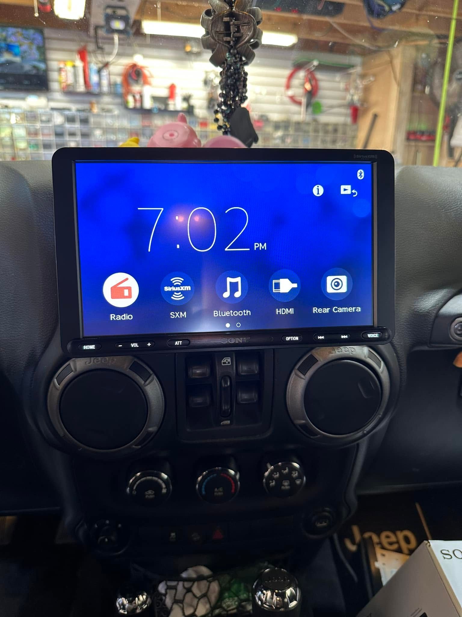 Car dashboard with a touchscreen showing 7:02, radio icons, and air vents below.