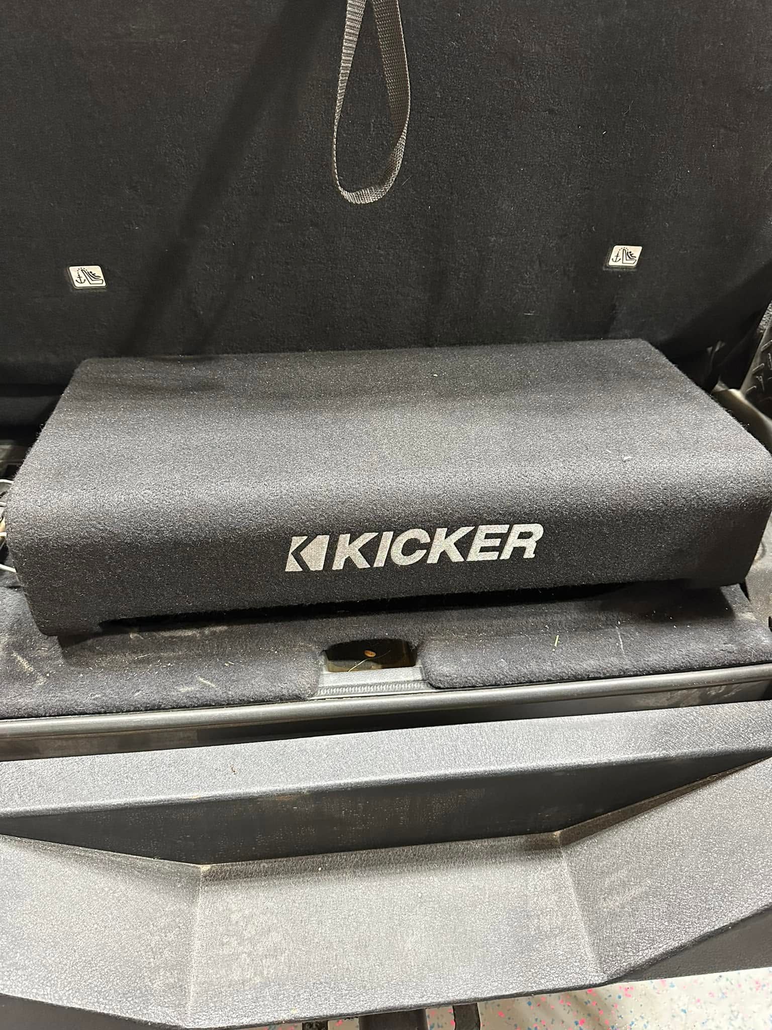Kicker subwoofer in a car trunk, black carpeted enclosure with logo visible.