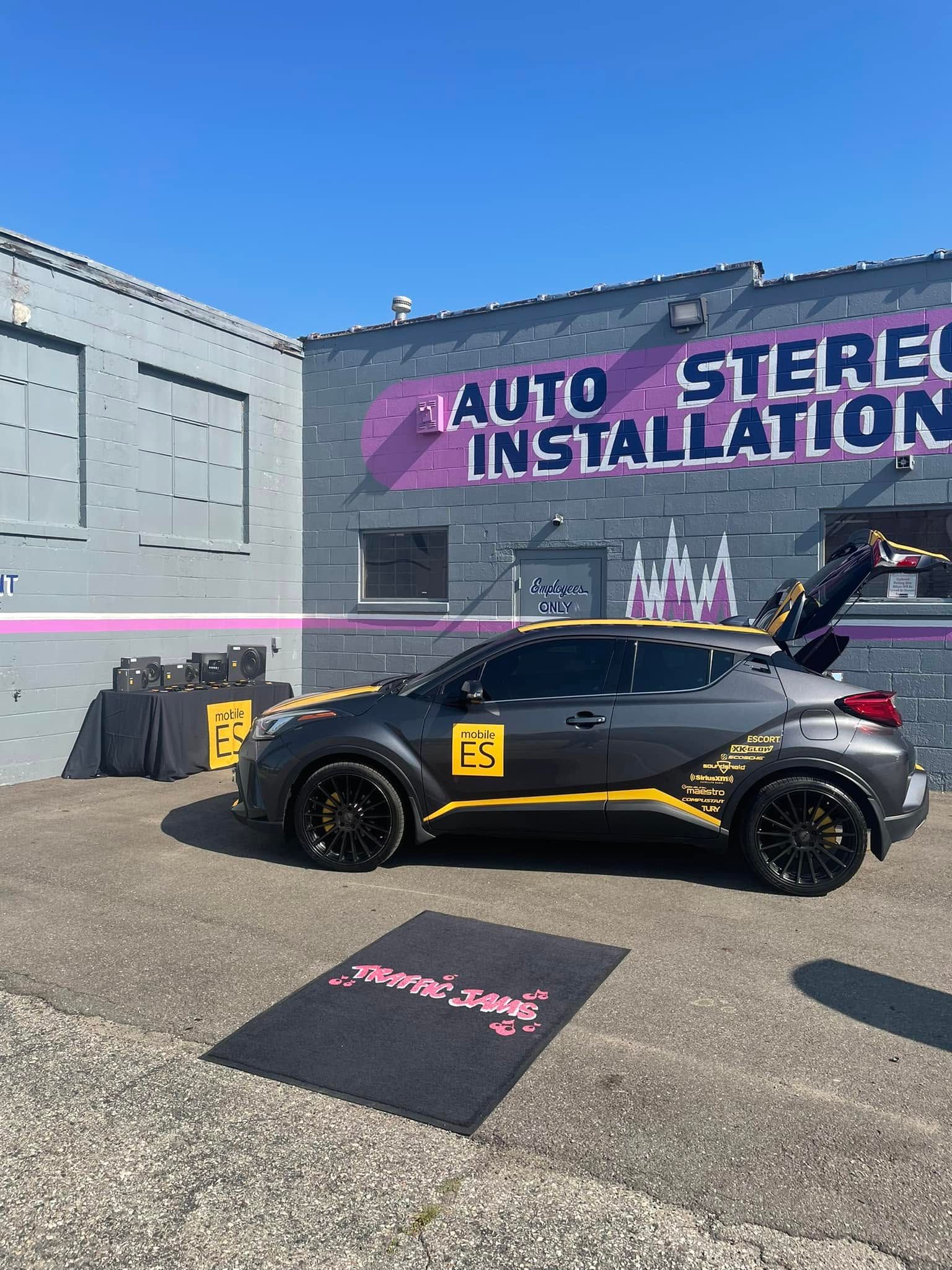Black convertible with gold accents parked outside an auto stereo installation shop.