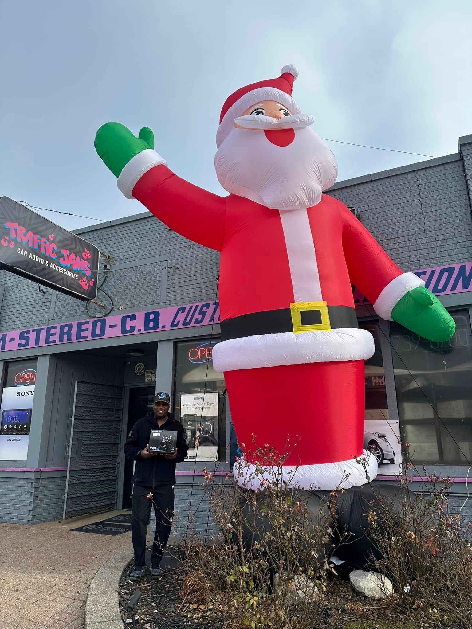 Person standing beside a giant inflatable Santa Claus outside a storefront.