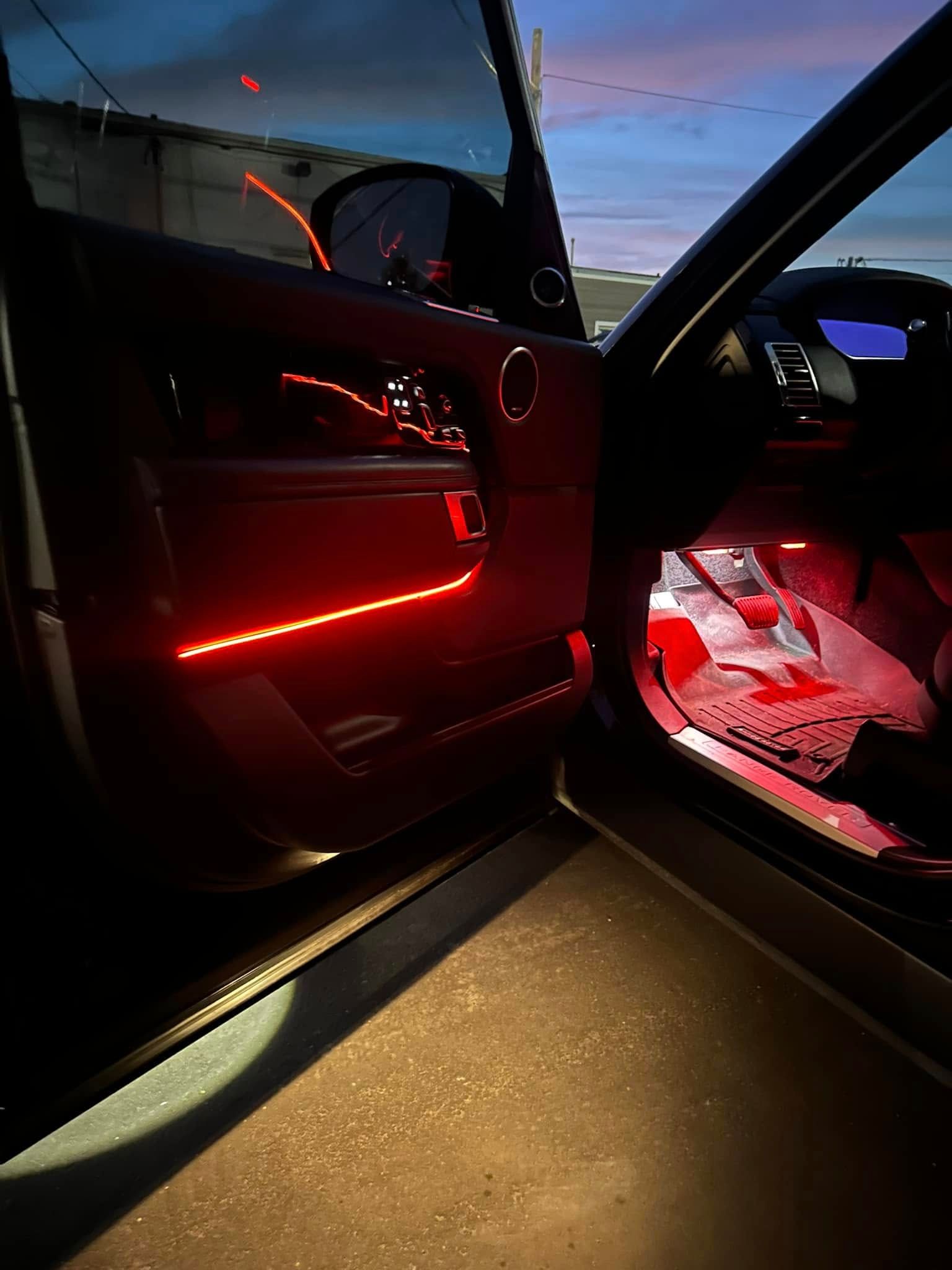 Open car door at dusk with red interior lights illuminating the cabin and floor.