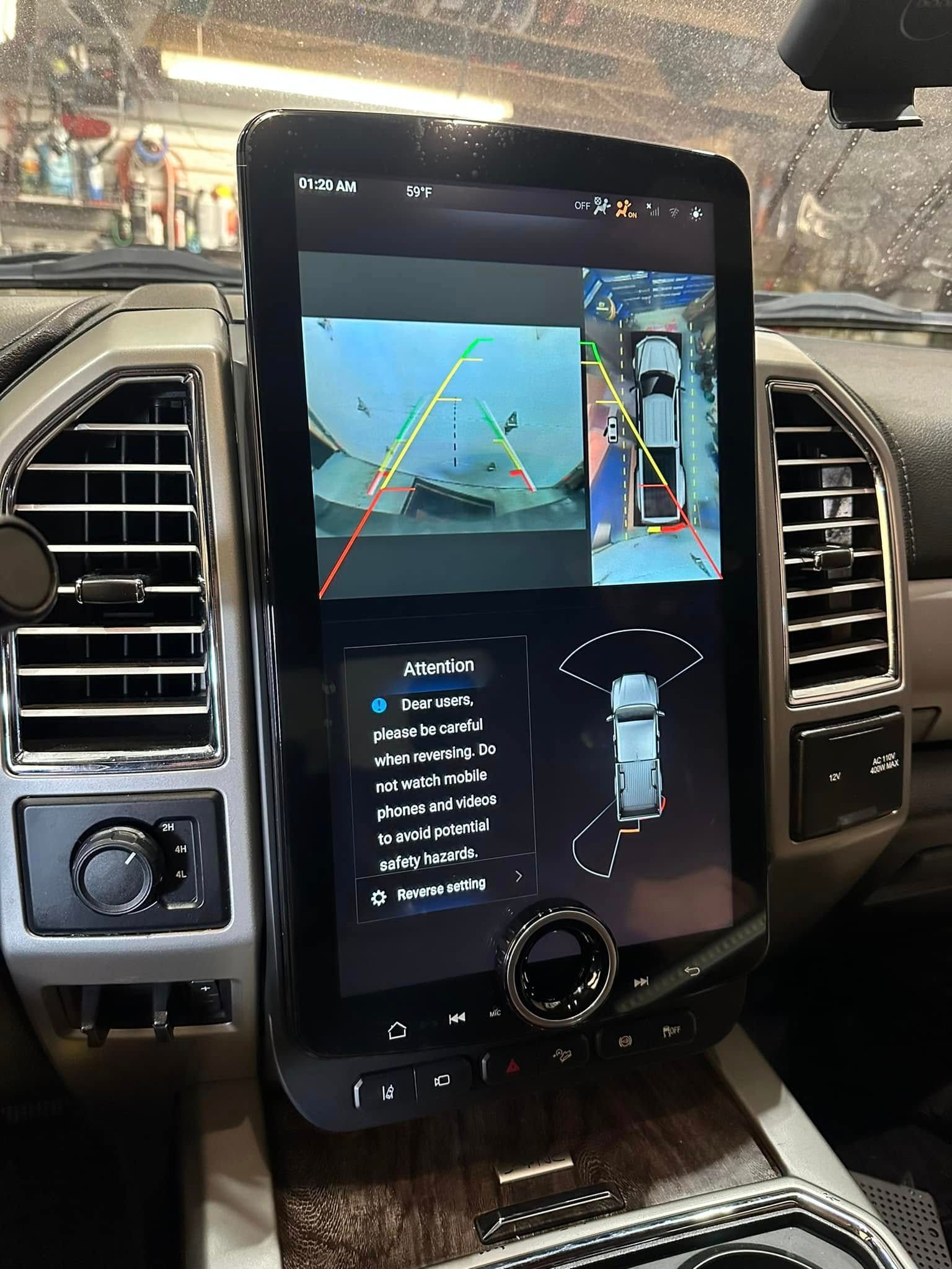 Car dashboard center screen showing backup camera view with parking guidelines and vehicle icons