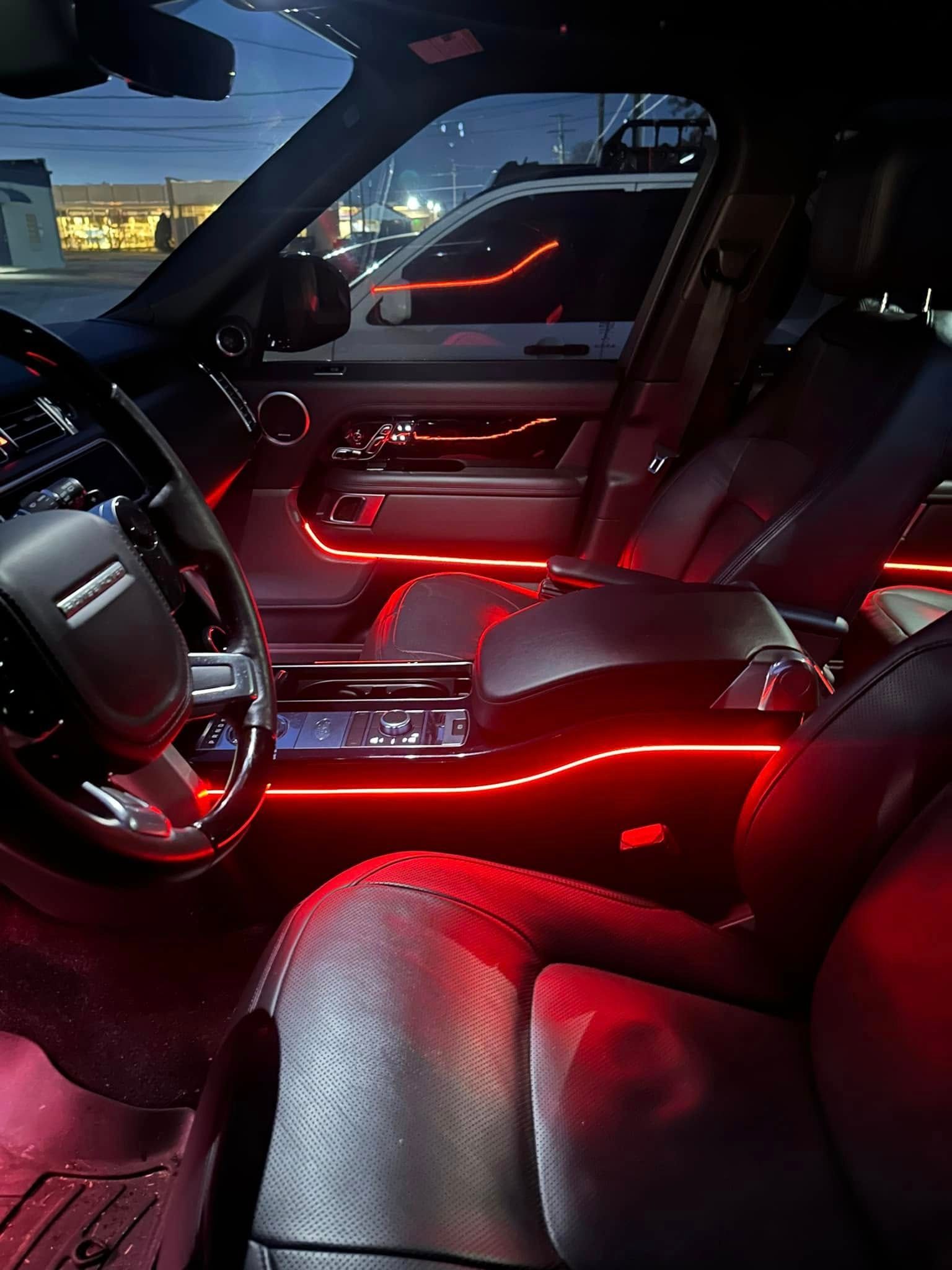 Car interior with red ambient lighting, showing the front seats, dashboard, and steering wheel at dusk.