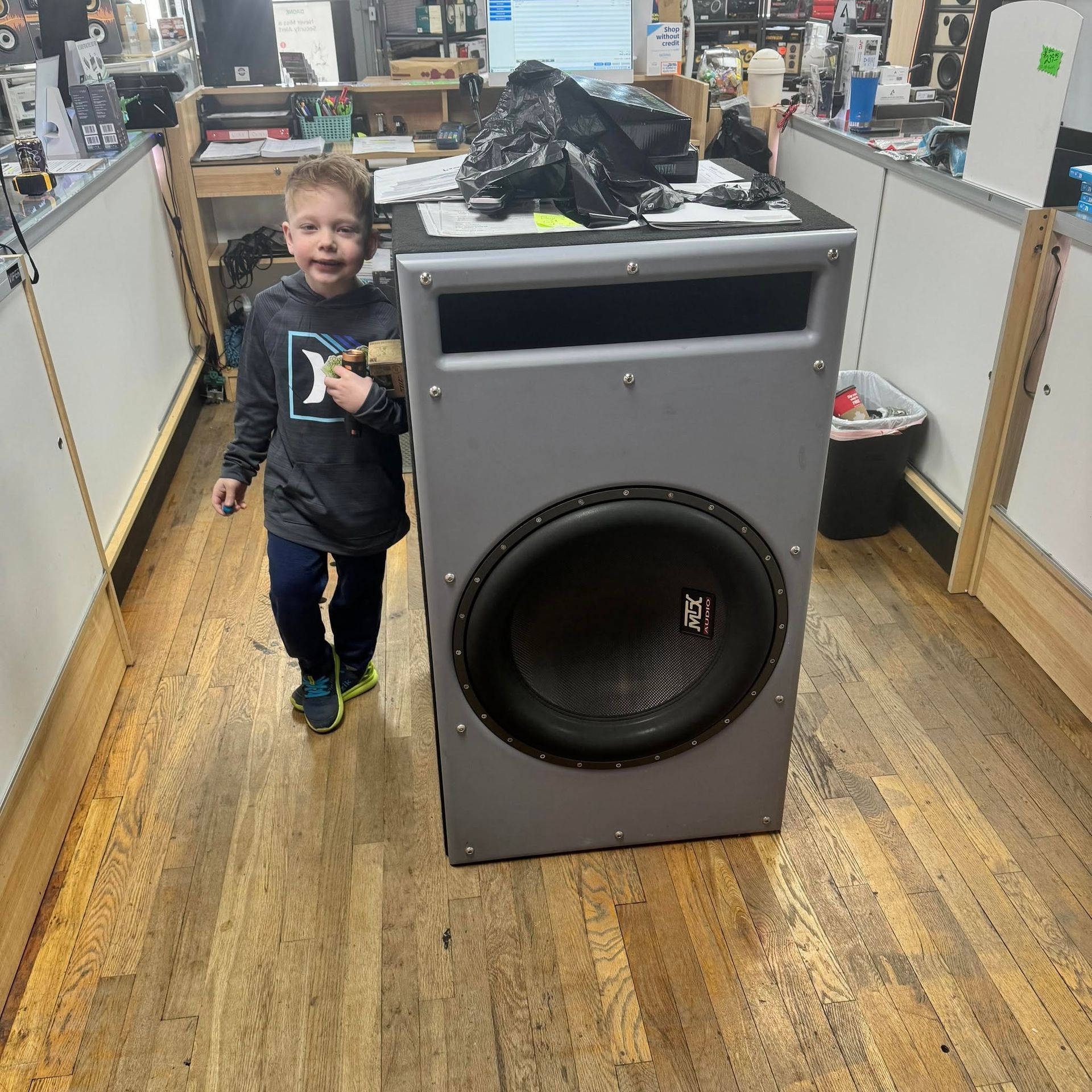 Child standing beside a large gray speaker cabinet in a store aisle
