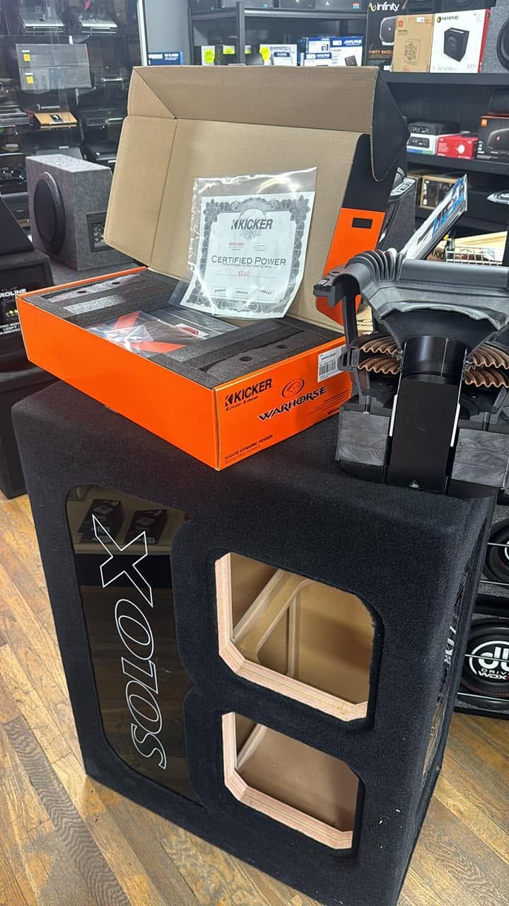 Open cardboard box with orange packaging on a black speaker cabinet in a shop aisle