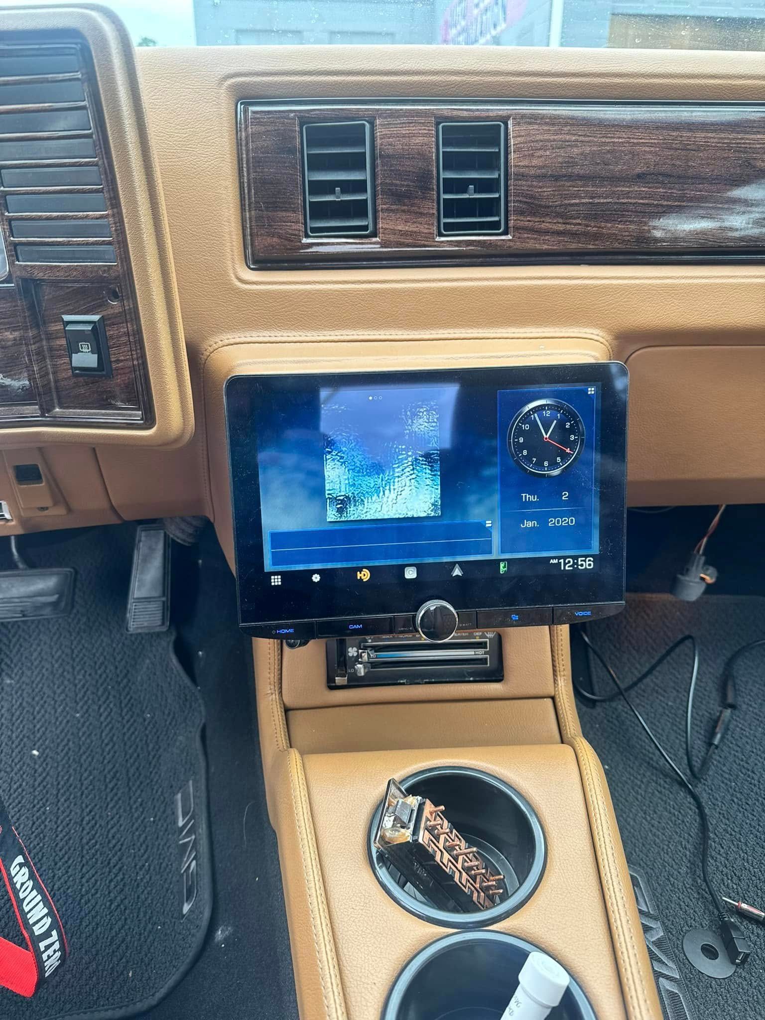 Car dashboard with a central touchscreen, air vents, and cup holder in a tan interior.