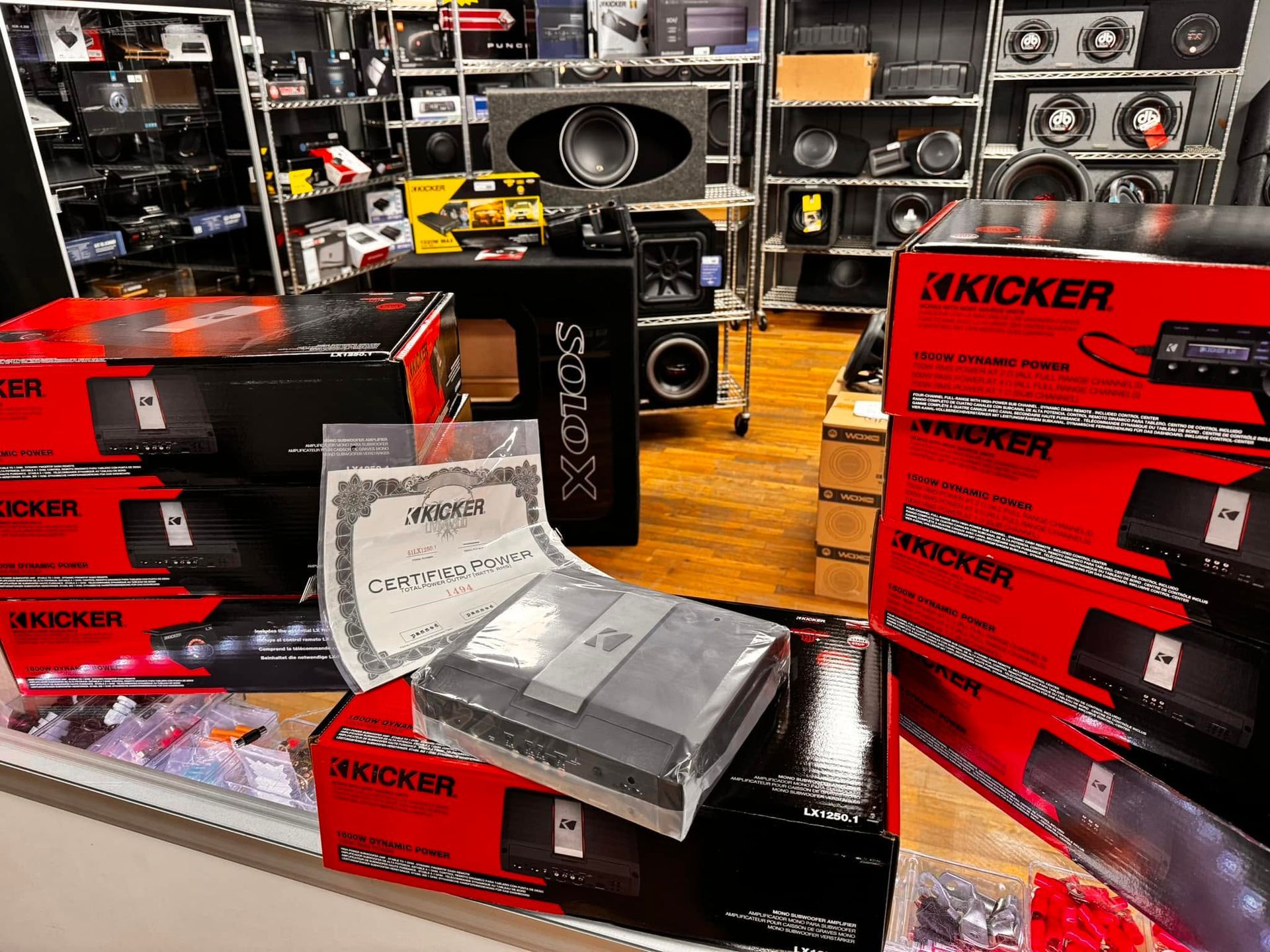 Kicker car audio display with stacked red boxes, speakers, and amplifier equipment in a shop