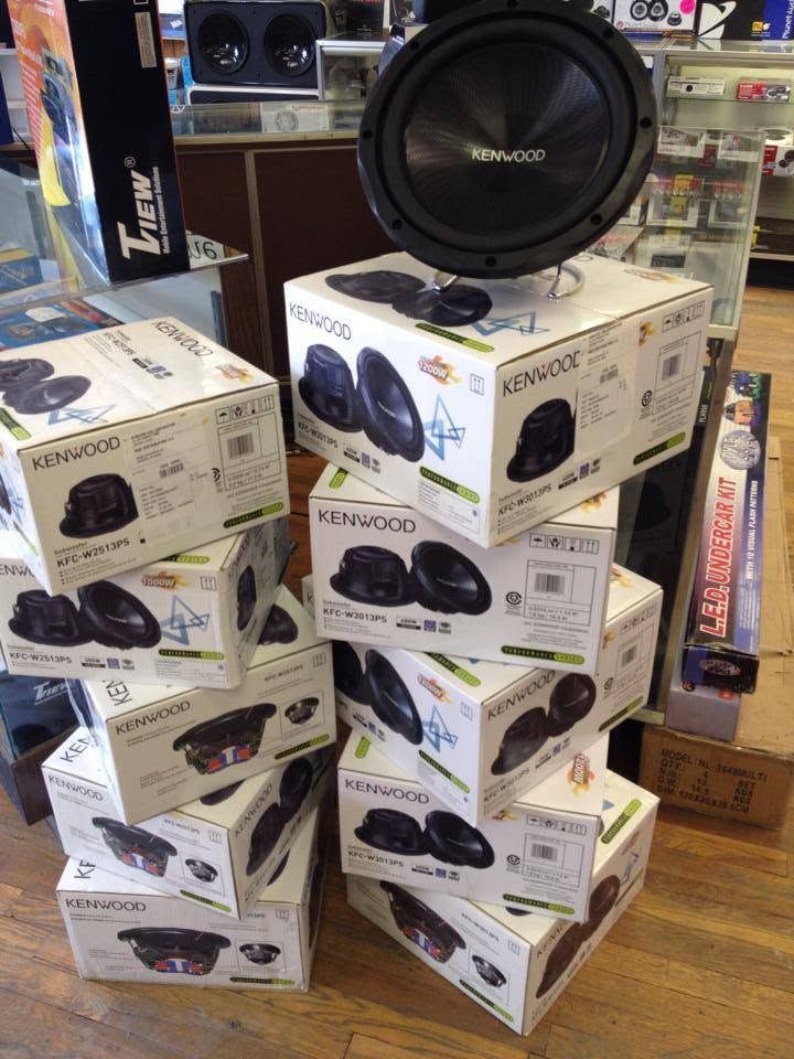 Stack of Kenwood speaker boxes in a store display with a large subwoofer on top.