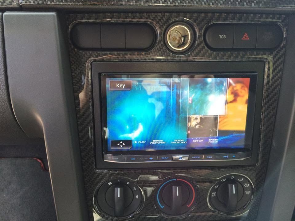 Car dashboard with a touchscreen displaying a colorful app interface and climate control knobs below.
