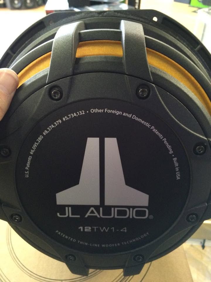 Close-up of a JL Audio 12-inch subwoofer with black cone and silver logo, held by a hand