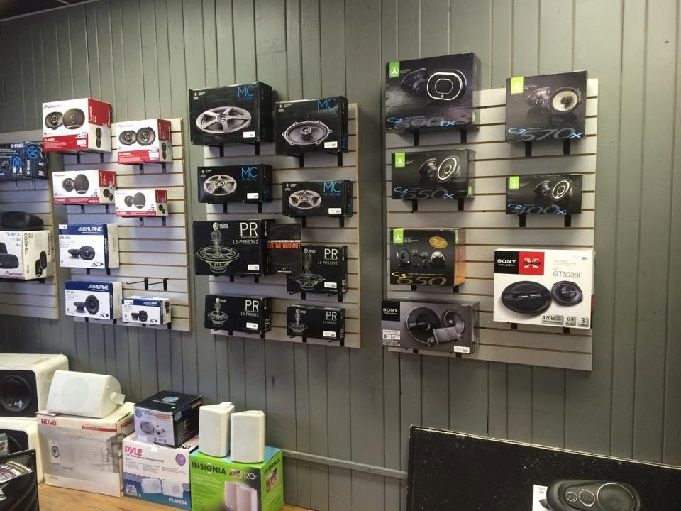 Display wall of boxed electronics in a retail store, mostly black and white packaging on gray slatwall.