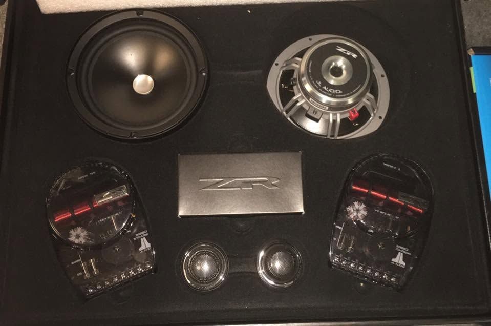 Car audio speaker set on a black display board, with subwoofers, tweeters, and a center logo plate.