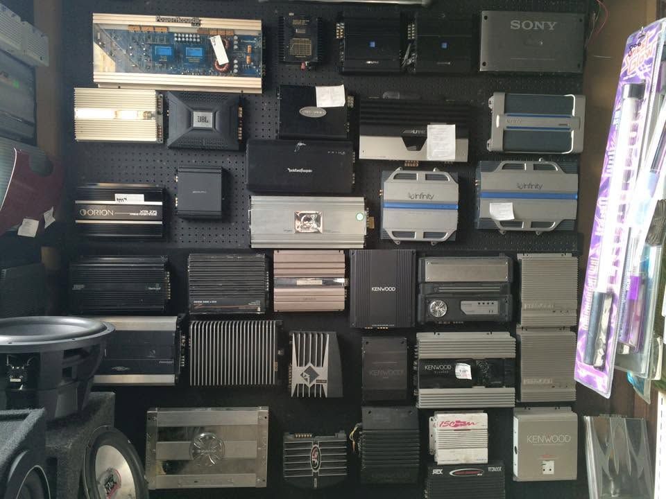 Wall of stacked electronic devices and audio gear on shelves, mostly black and gray.