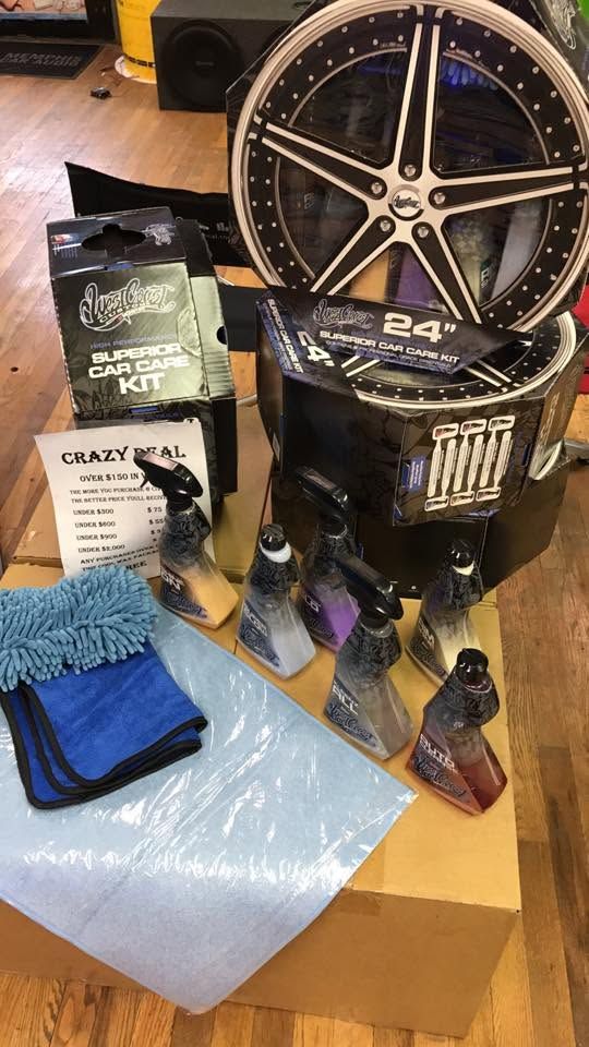 Car parts and detailing supplies on a cardboard box, including a wheel, car cleaner, towels, and bottles