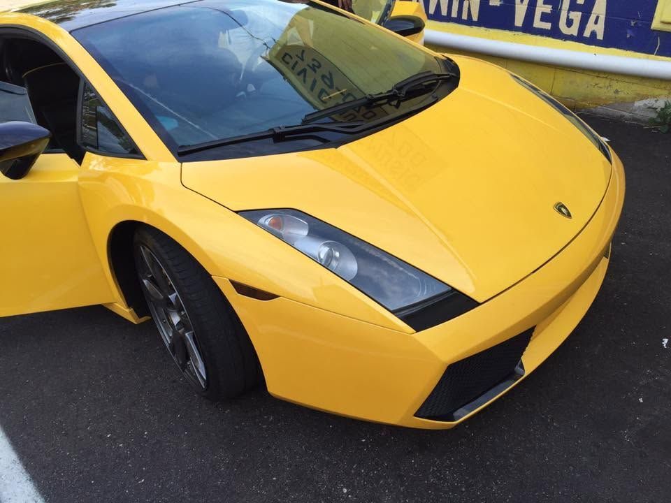 Yellow sports car parked outdoors, front-left view, with a blue-and-yellow barrier in the background