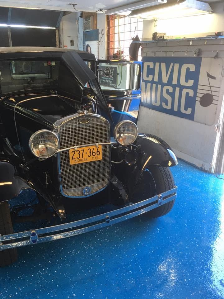 Vintage black car in a garage with a bright blue floor and a Civic Music sign behind it