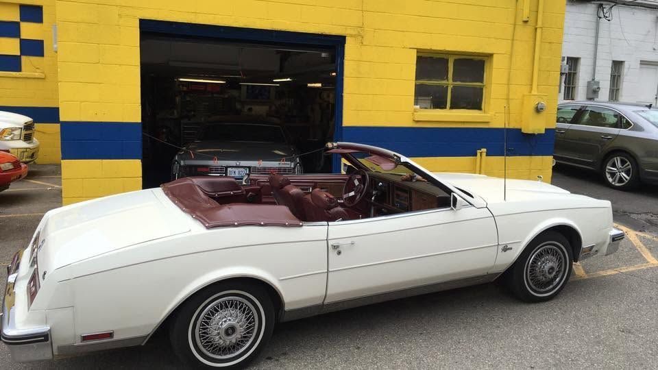 White convertible car parked beside a yellow building and garage doorway