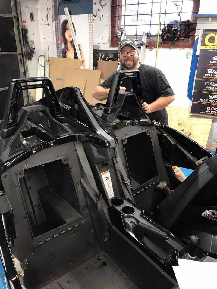 Person smiling beside a black vehicle frame in a workshop