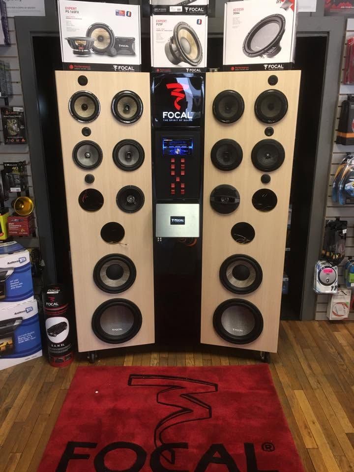 Focal speaker display with tall beige floor speakers, central audio unit, and red Focal rug in a shop.
