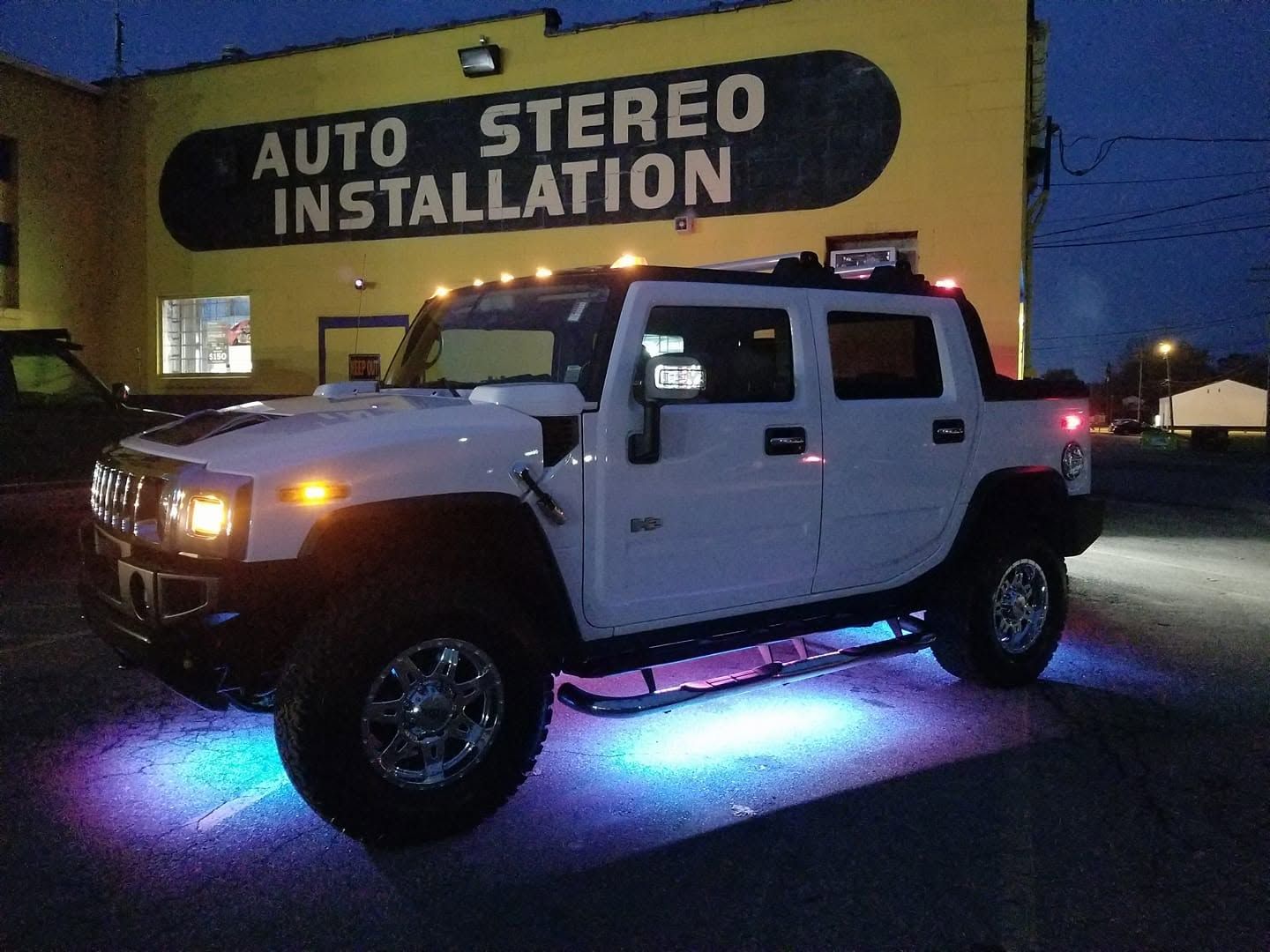 White Hummer with colorful underglow parked outside Auto Stereo Installation at dusk