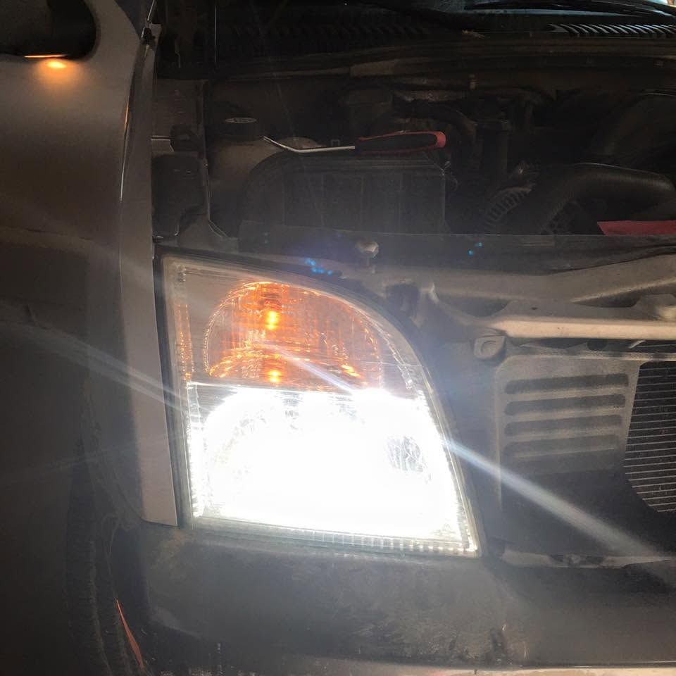 Close-up of a car front with the headlight and amber turn signal illuminated in the dark
