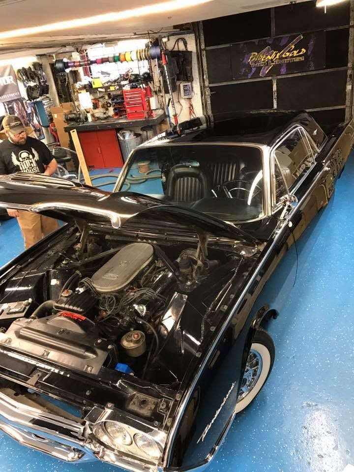Black classic car with hood open in a garage, showing the engine bay and chrome trim.