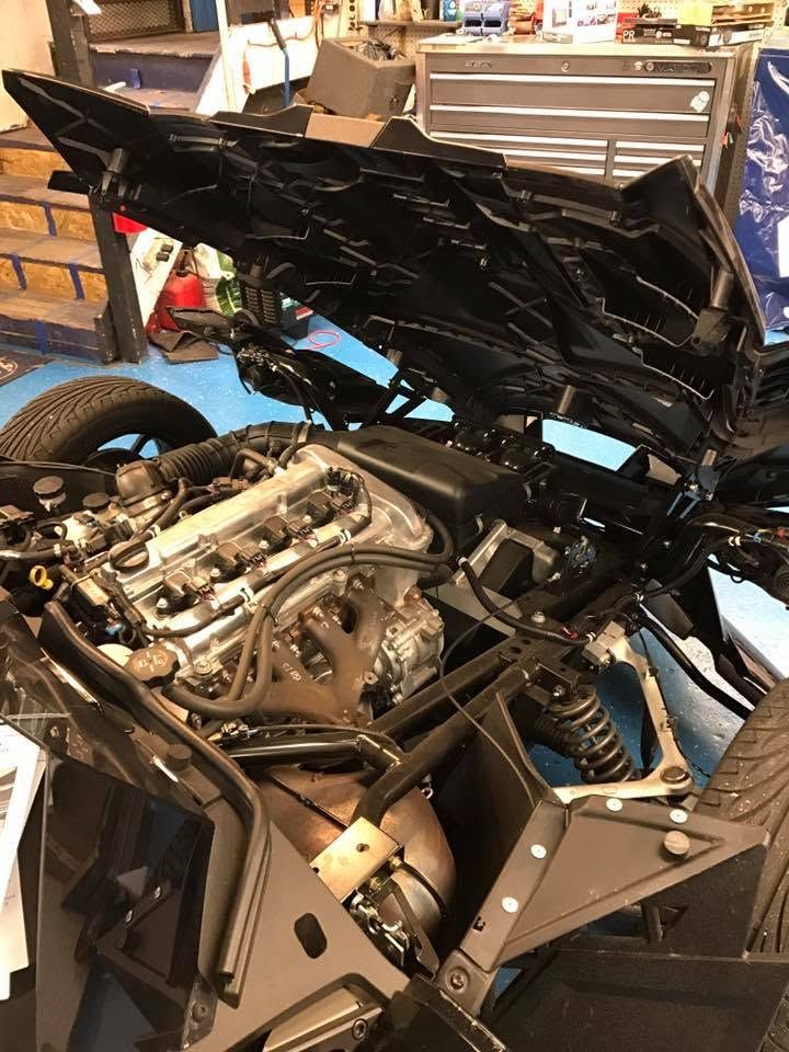 Black sports car with rear hatch open, exposing the engine in a garage or workshop.