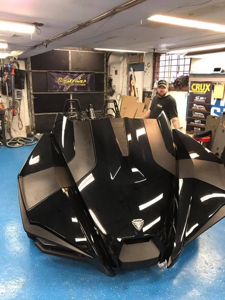 Black futuristic sports car with sharp angular body in a garage, with a person standing behind it.