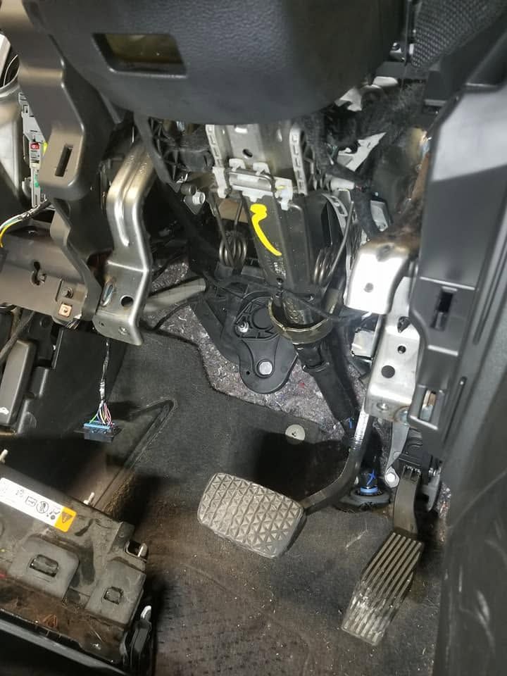Car footwell with exposed steering column, pedals, and wiring under the dashboard