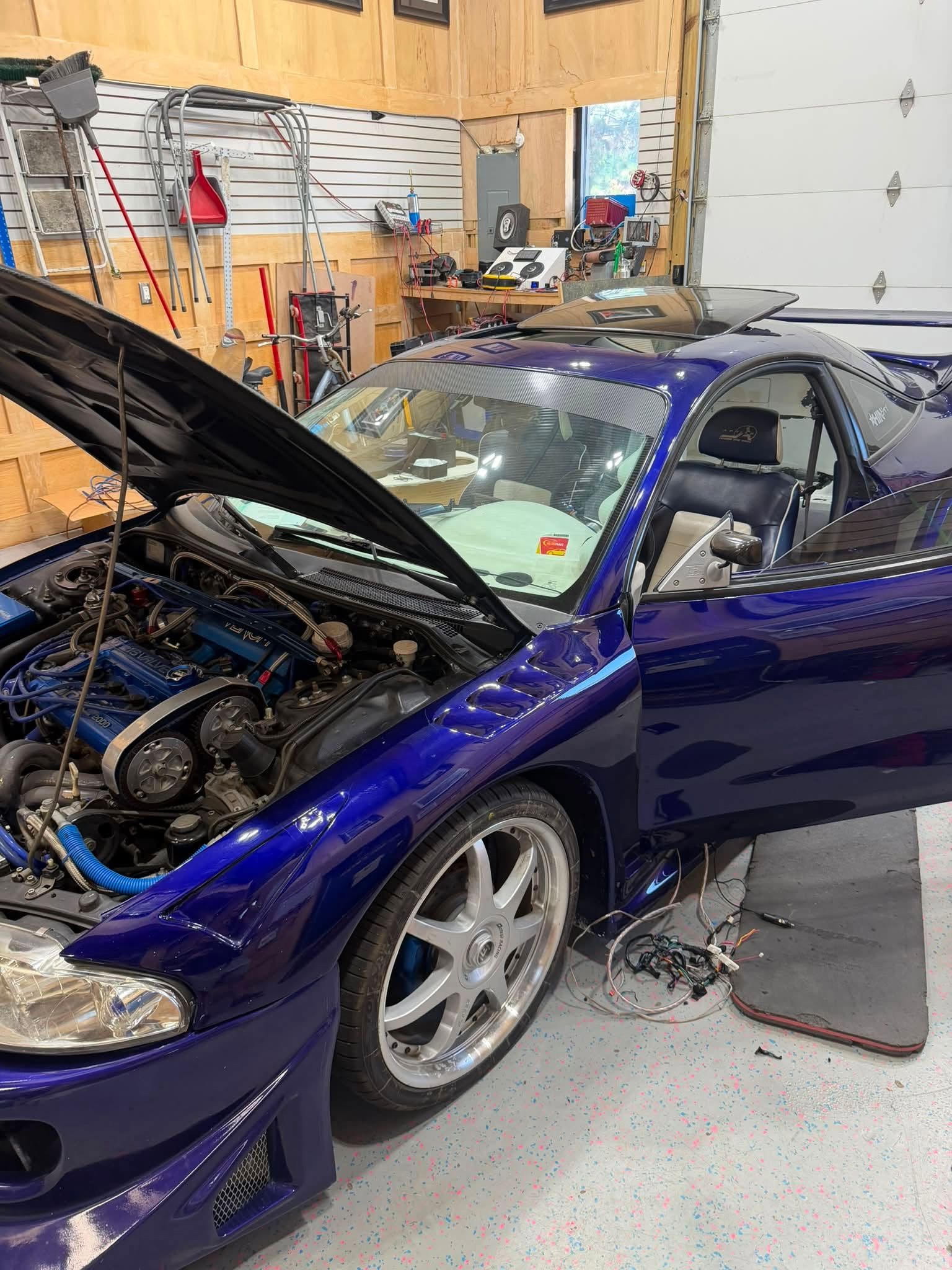 Blue sports coupe in a garage with hood open, exposing the engine and front damage.