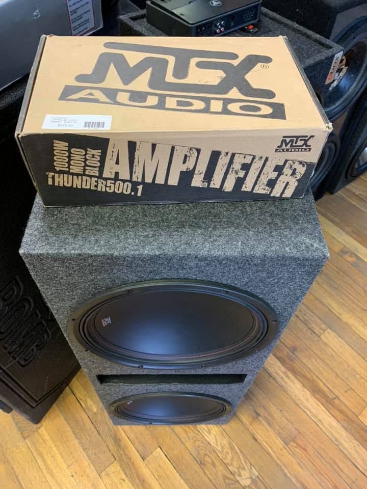 Speaker cabinet with a large subwoofer topped by an MTX Audio box, likely in a car audio shop.