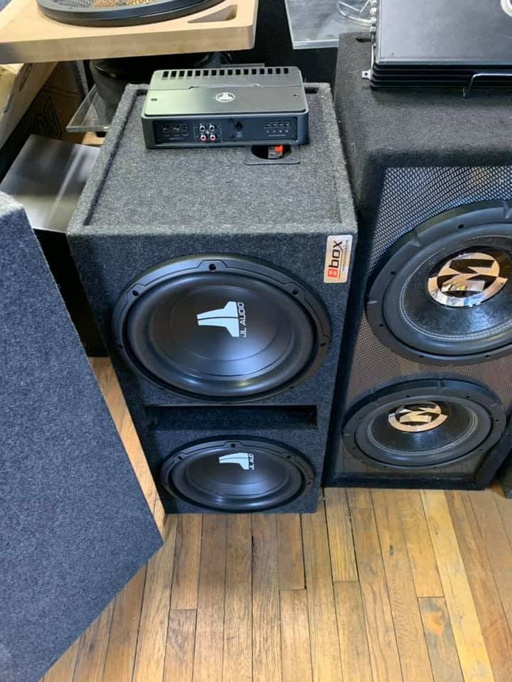 Stacked black subwoofers with a small amplifier on top in a music store.
