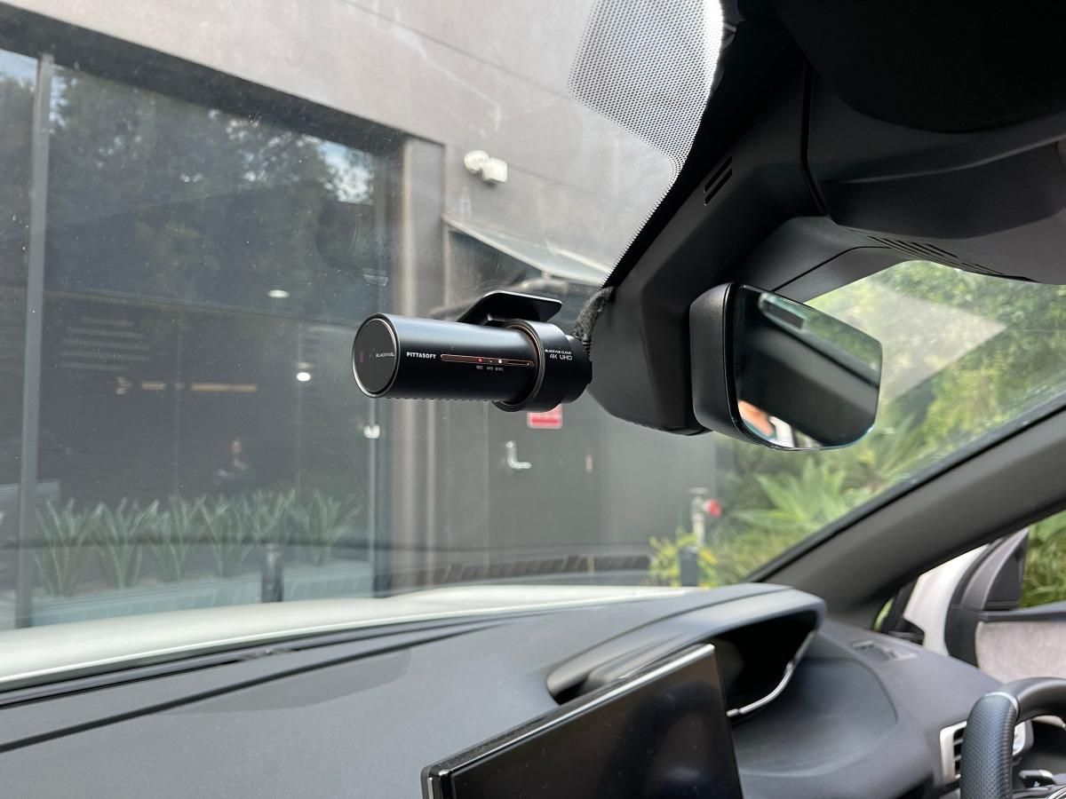 Dash-mounted cylindrical camera inside a car, aimed at a sidewalk and building outside the windshield
