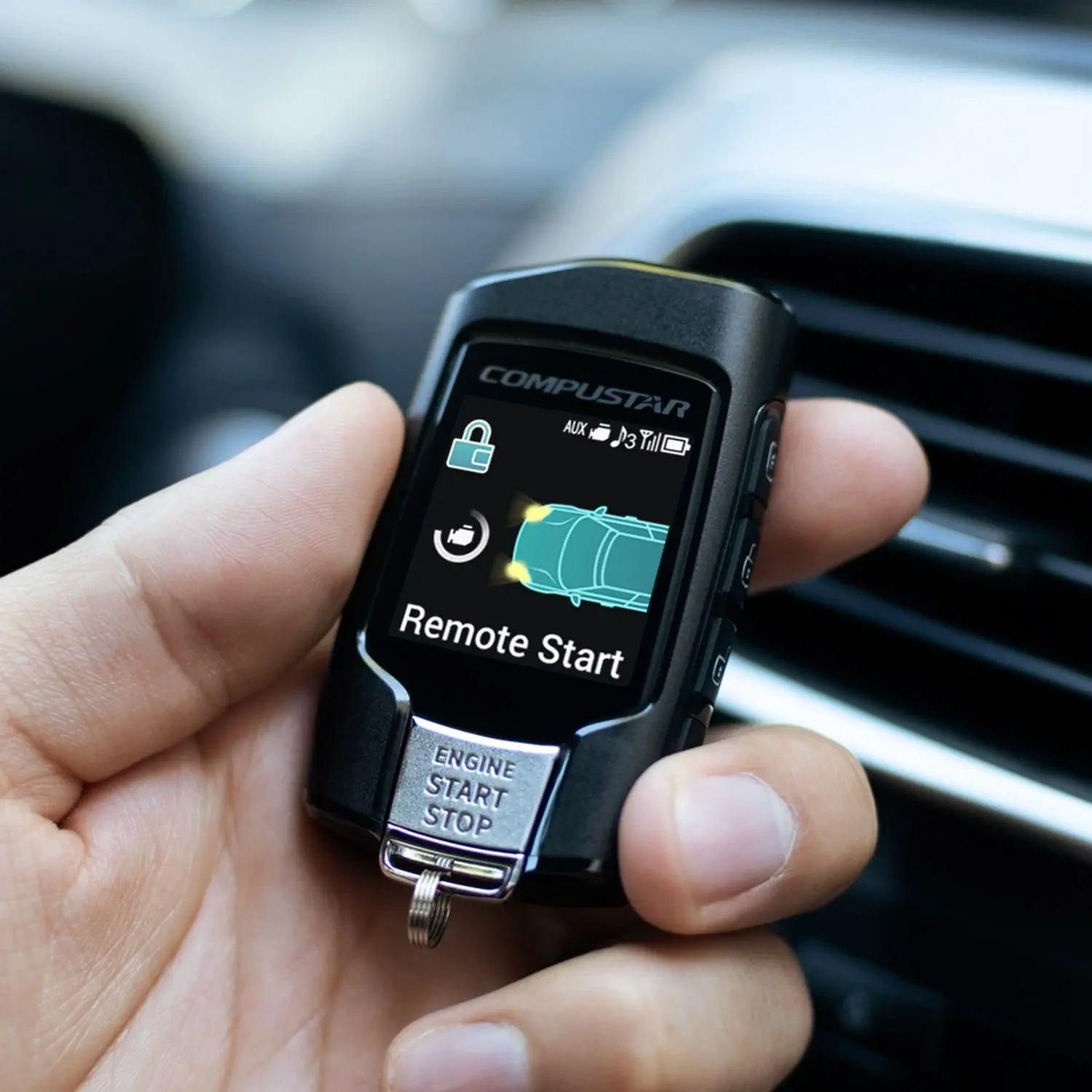 Hand holding a black car remote start key fob with a small display.