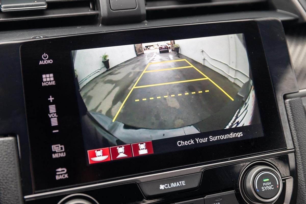 Car backup camera view with yellow parking guidelines and “Check Your Surroundings” warning on the screen