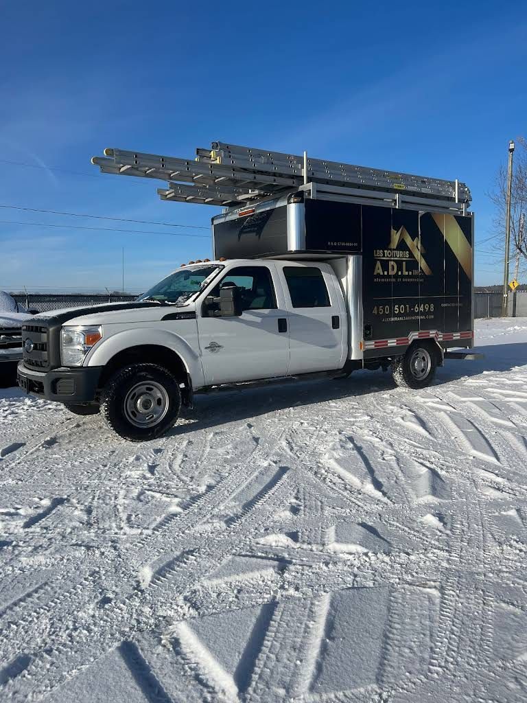 White utility truck with ladder racks parked on snowy ground under a clear blue sky.