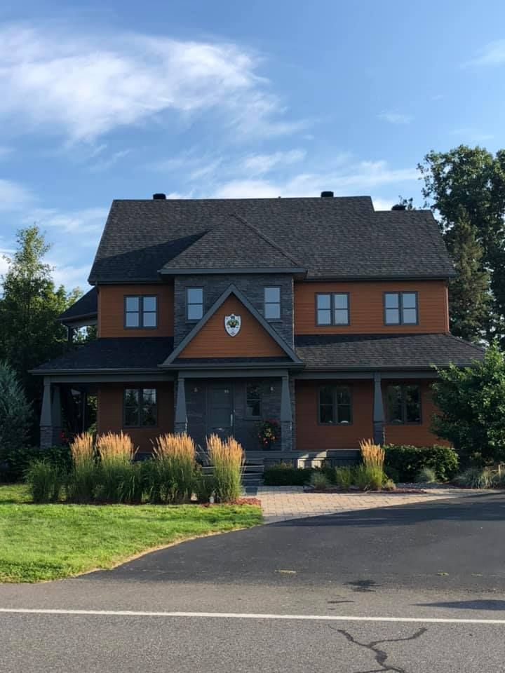 Two-story brick house with a dark roof, front porch, and landscaped yard under a blue sky