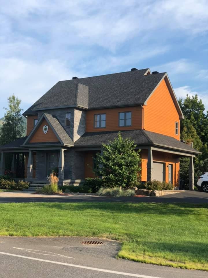 Two-story orange house with dark roof, front porch, and green lawn under a blue sky