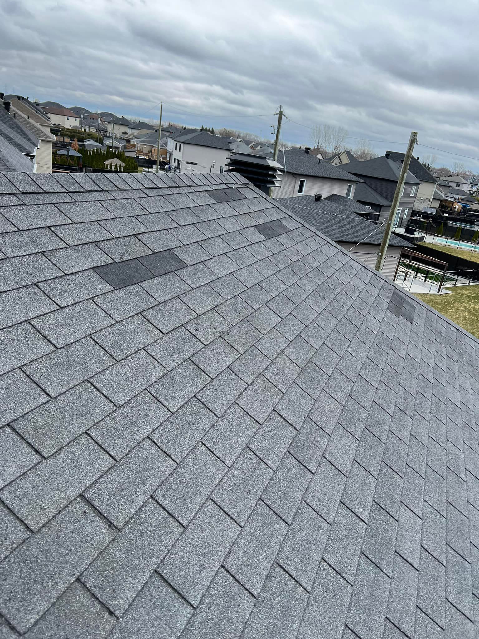 Gray shingled rooftop overlooking a town under a cloudy sky