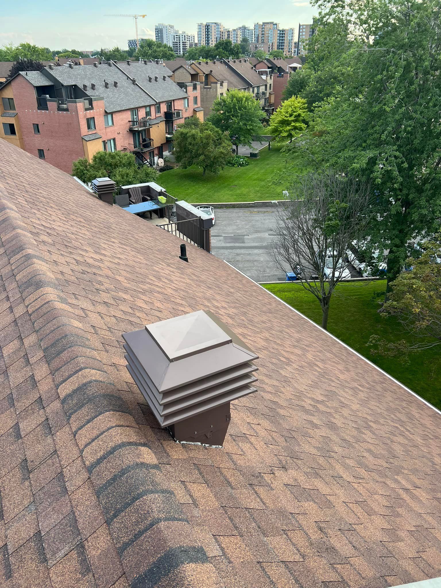 Rooftop view of brick townhouses, green trees, and a distant city skyline under a cloudy sky.