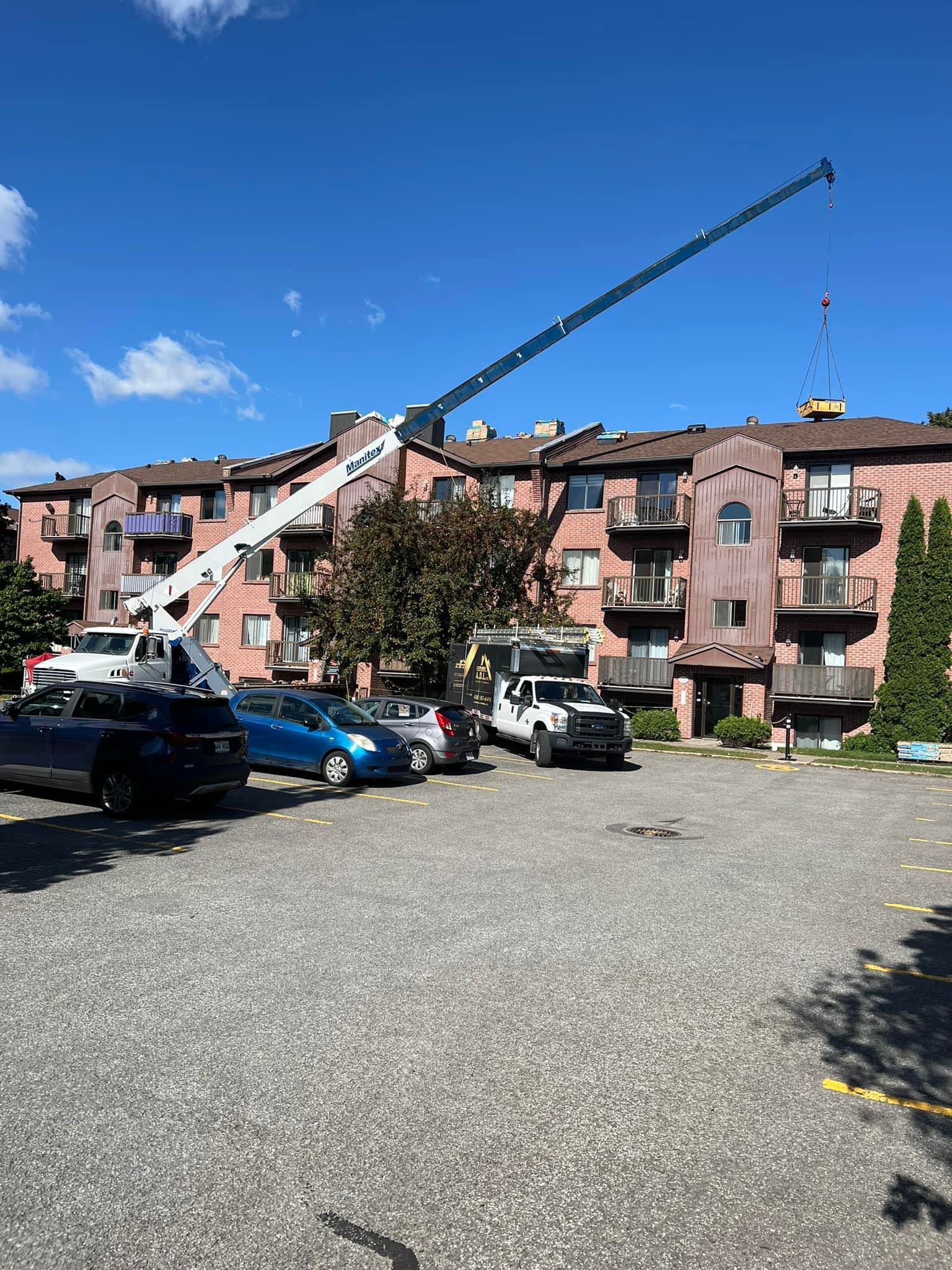 Construction crane lifting a load beside a pink apartment building under a bright blue sky