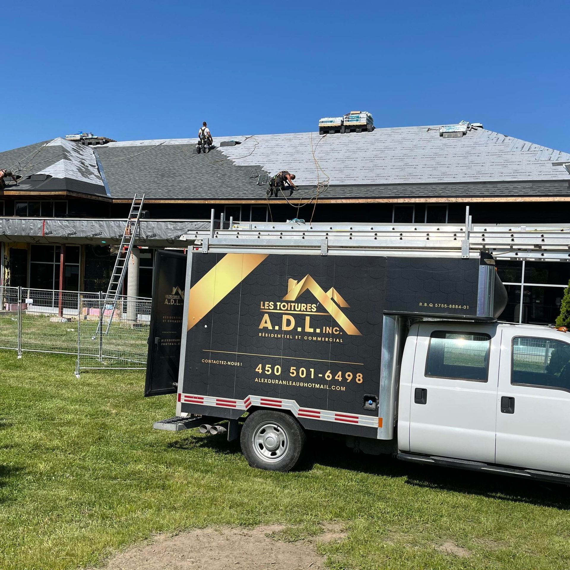 White utility truck parked on grass beside a house with workers on the roof during repairs