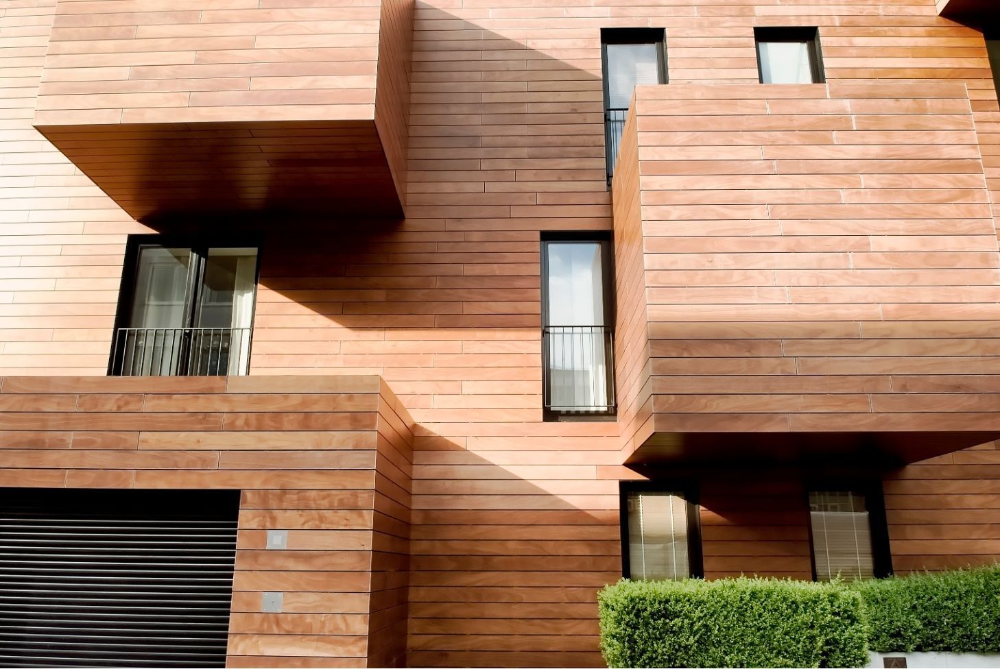 Modern copper-toned house facade with geometric windows and a hedge in front