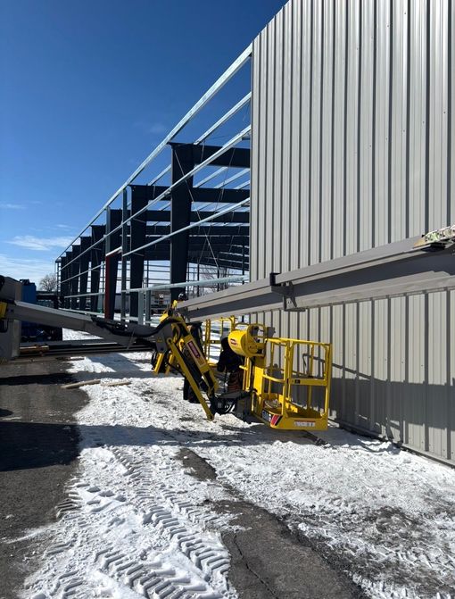 Yellow lift beside steel-framed building under construction on a snowy site