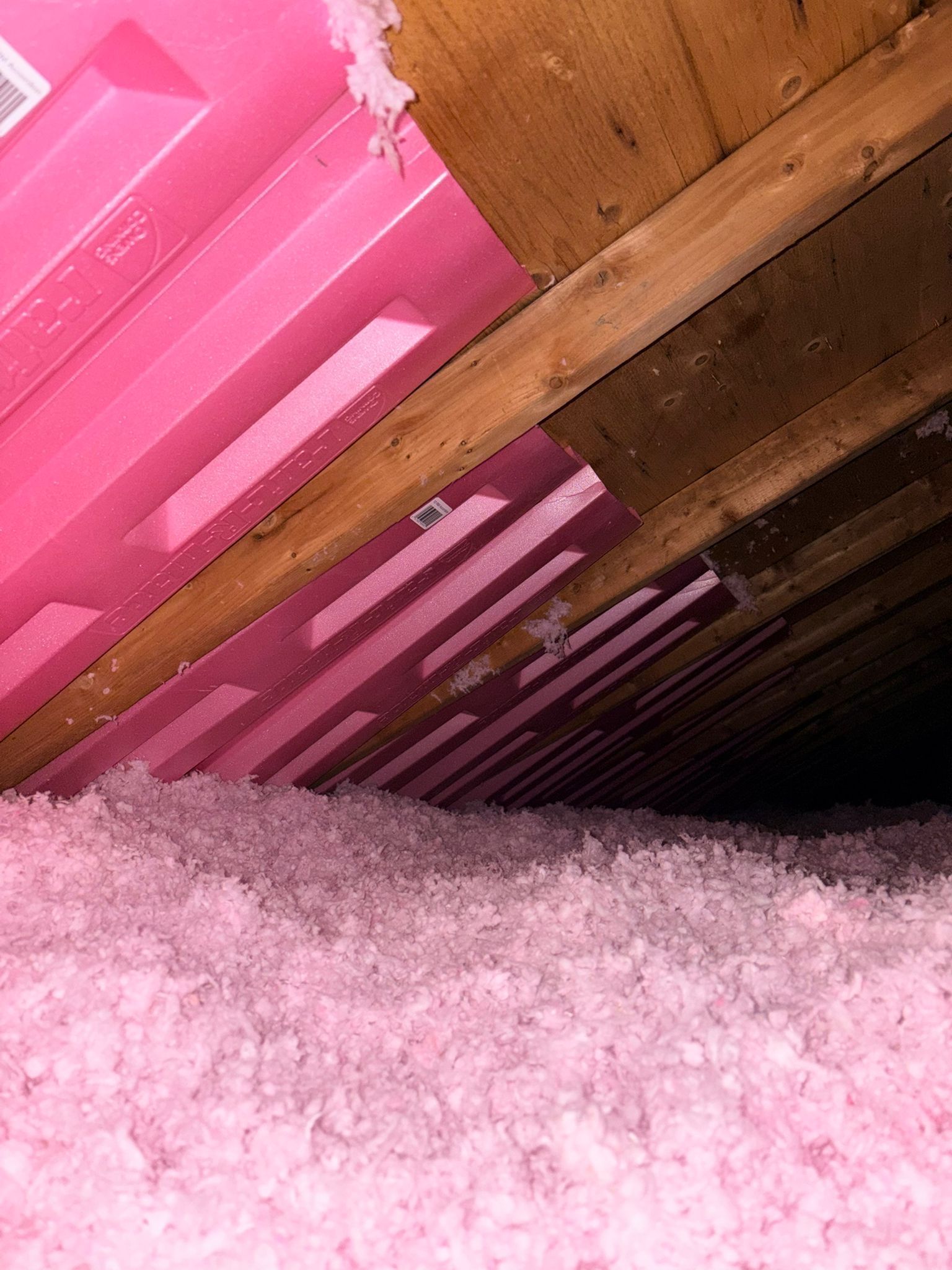 Pink insulation beneath wooden roof beams and a pink plastic panel.