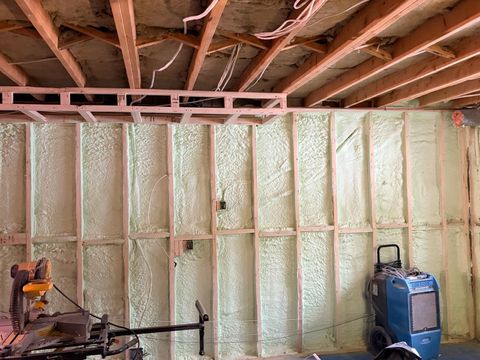 Basement with exposed wood beams, spray foam insulation, and construction tools on the floor