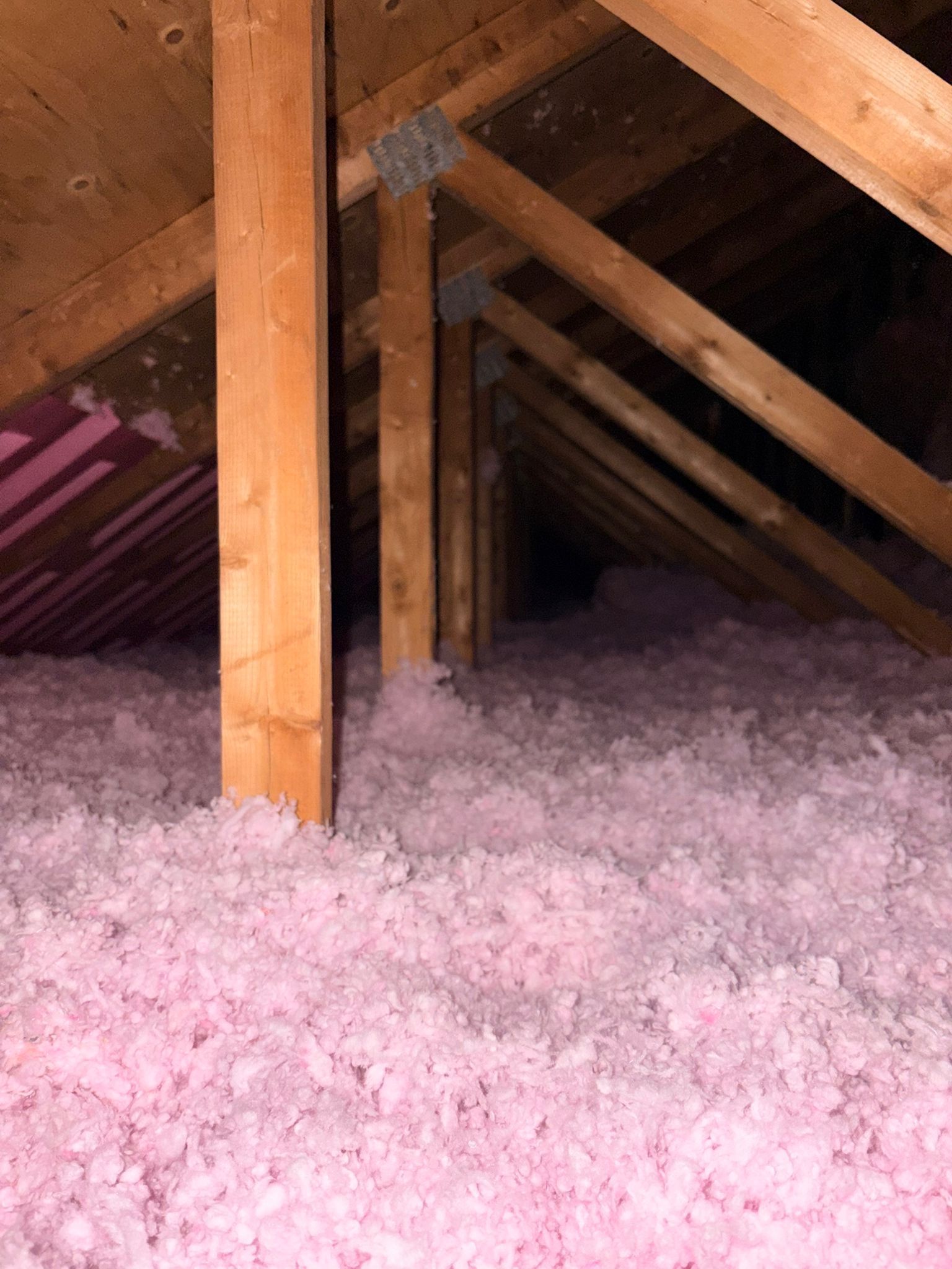 Attic with exposed wooden beams and pink blown-in insulation on the floor
