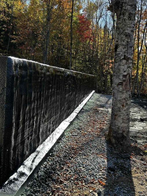 Black waterfall beside a gravel path in a wooded area with autumn leaves and a birch tree