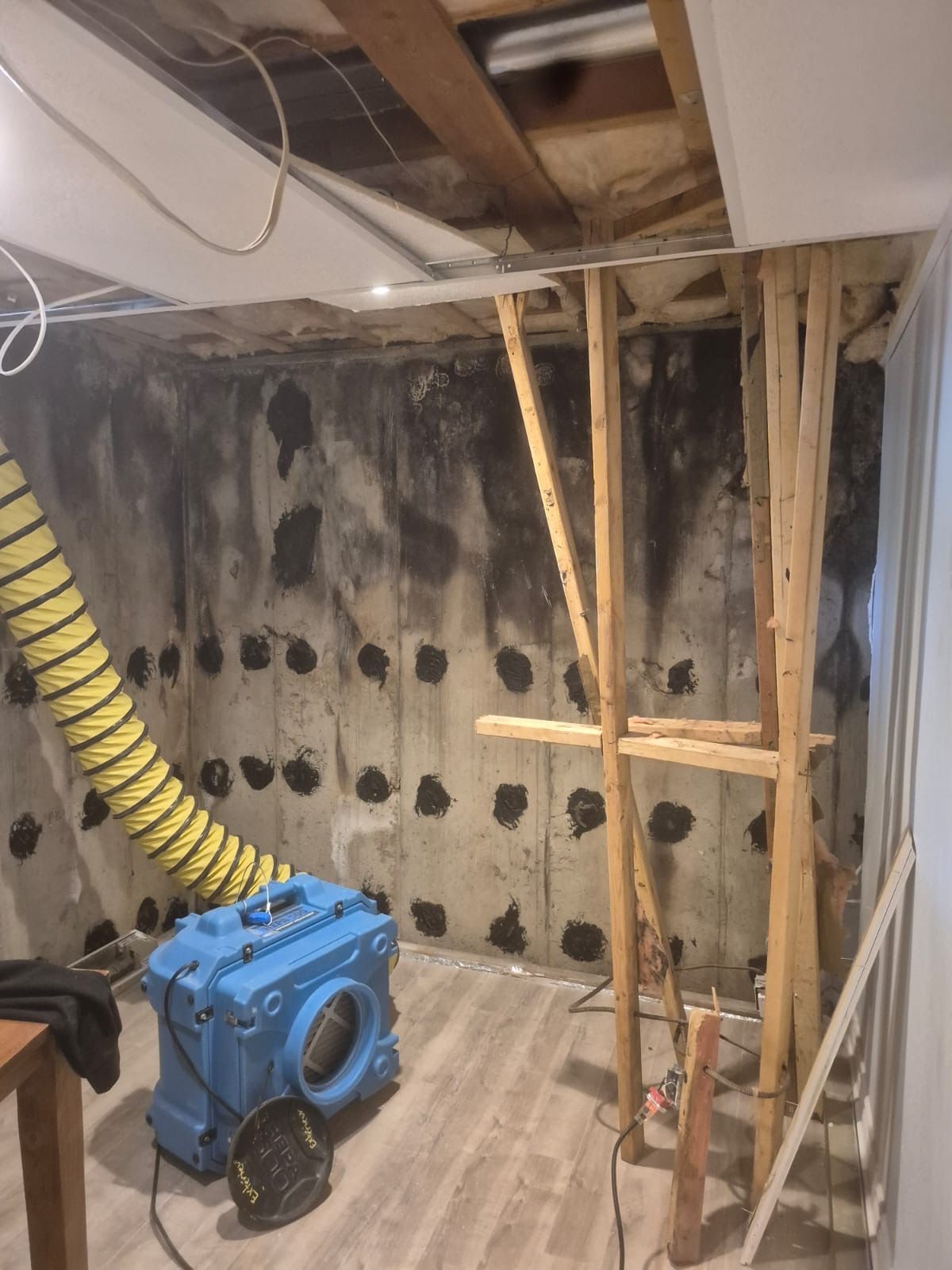Basement under construction with exposed framing, a blue machine, and a yellow ventilation hose