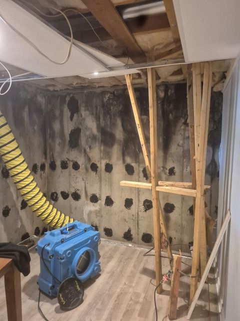 Basement under construction with exposed framing, a blue machine, and a yellow ventilation hose